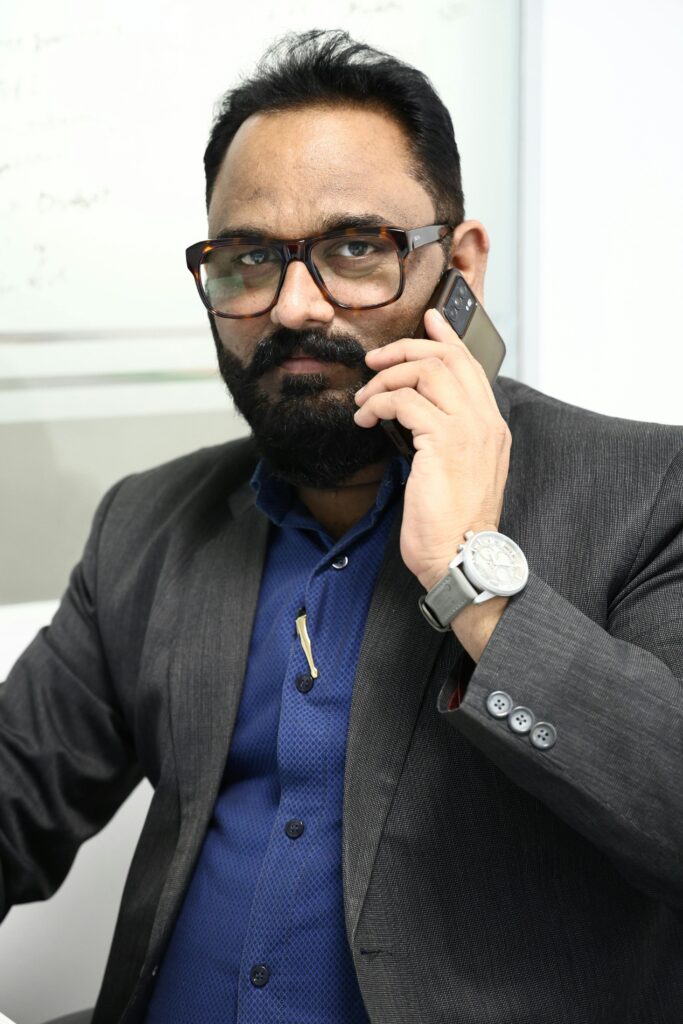 Confident businessman with beard and glasses speaking on mobile phone in office setting.